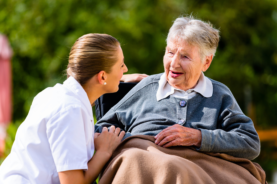 Nurse holding hands with senior woman sitting in wheelchair in garden of retirement home